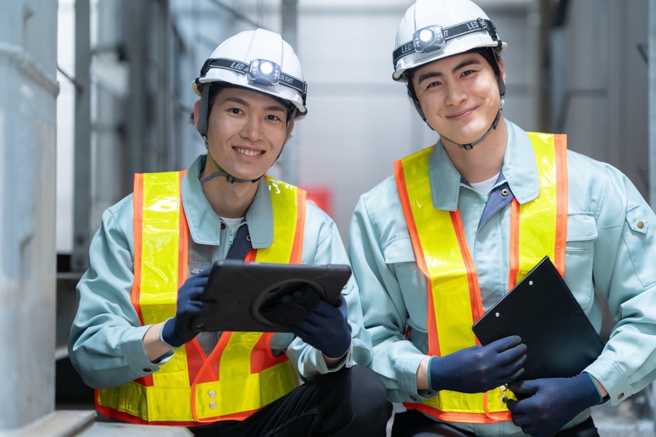 ヘルメットと安全ベストを着けた2人の作業者が、現場でタブレットを見ている